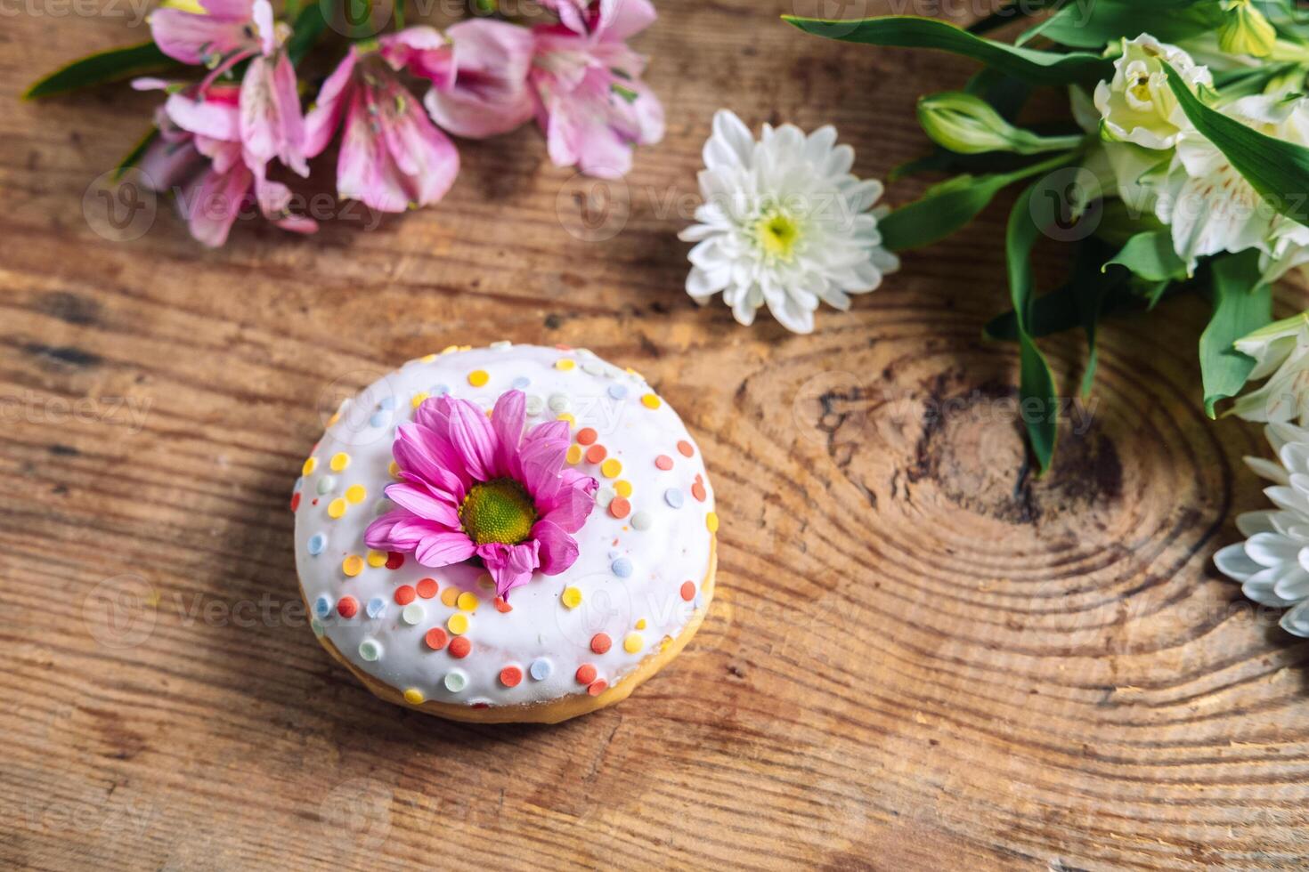 chamomile bud on top of a donut on a wooden background with a bouquet of alstroemerias. Delicate frame with pink flower photo
