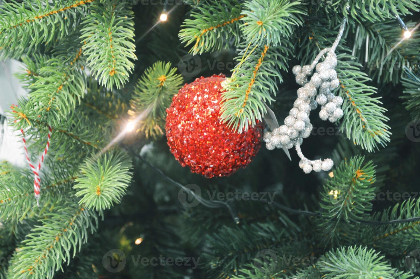Red shiny ball, colored baubles hanging on the branches of a Christmas tree. Holiday decor. Background. photo