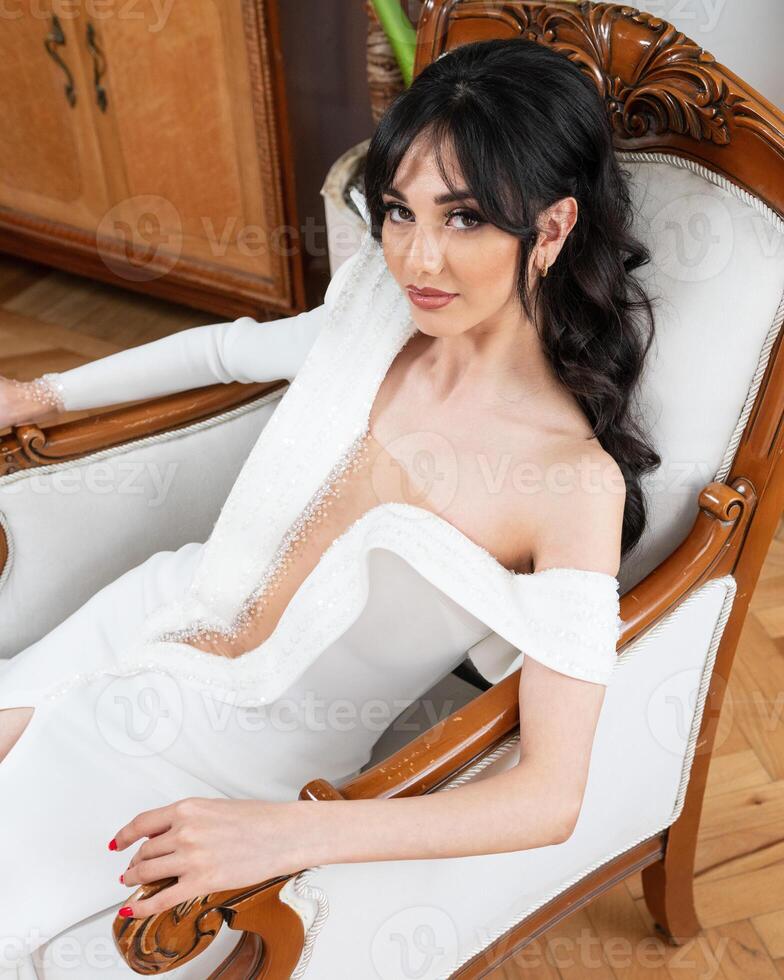 A woman in a white dress sits in a chair photo