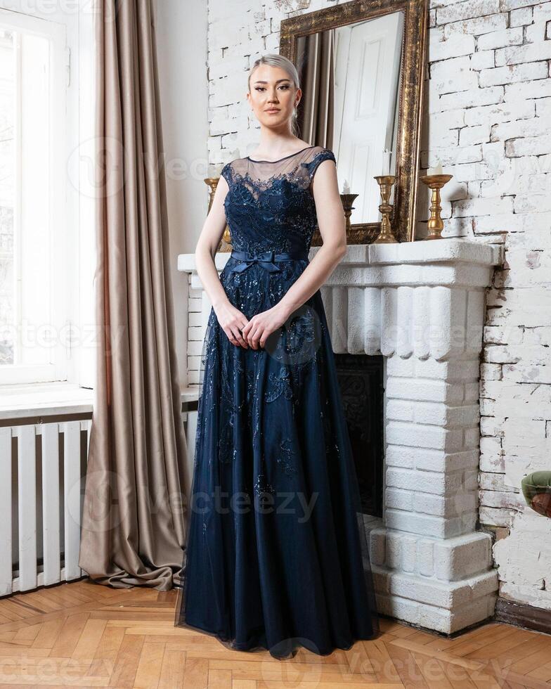 A woman in a blue dress stands in front of a fireplace photo