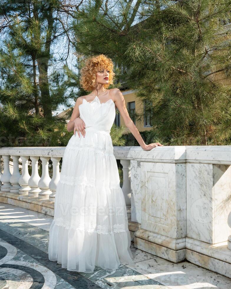A woman in a white dress stands in front of a house. photo