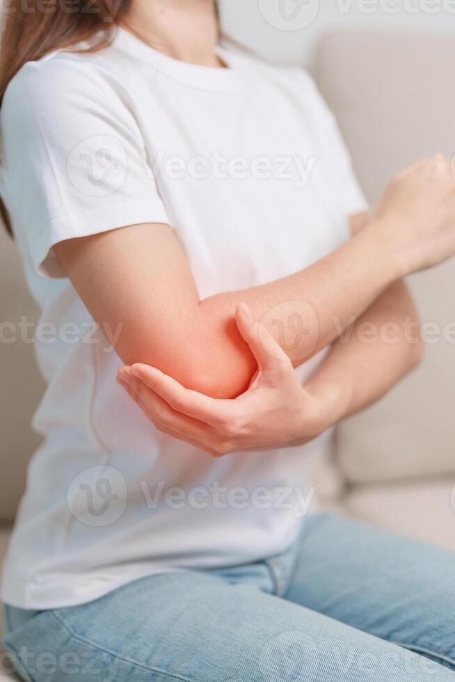 Woman having elbow ache during sitting on couch at home, muscle pain due to lateral epicondylitis or tennis elbow. injury, Health and medical concept photo