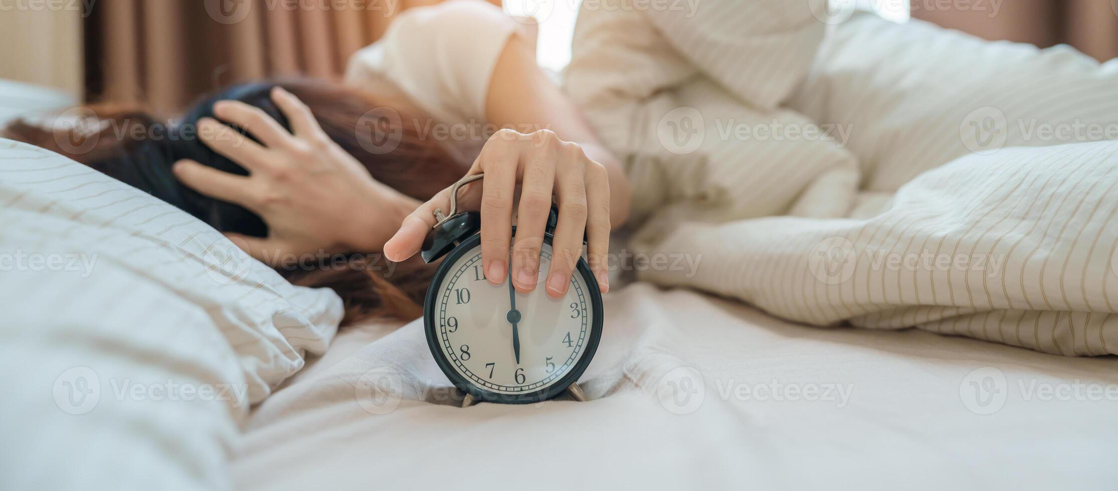 alarm clock and asian woman hand stop time in bed while sleeping, young adult female wake up late in the early morning. Relaxing , sleepy, daily routine and have a nice day concepts photo