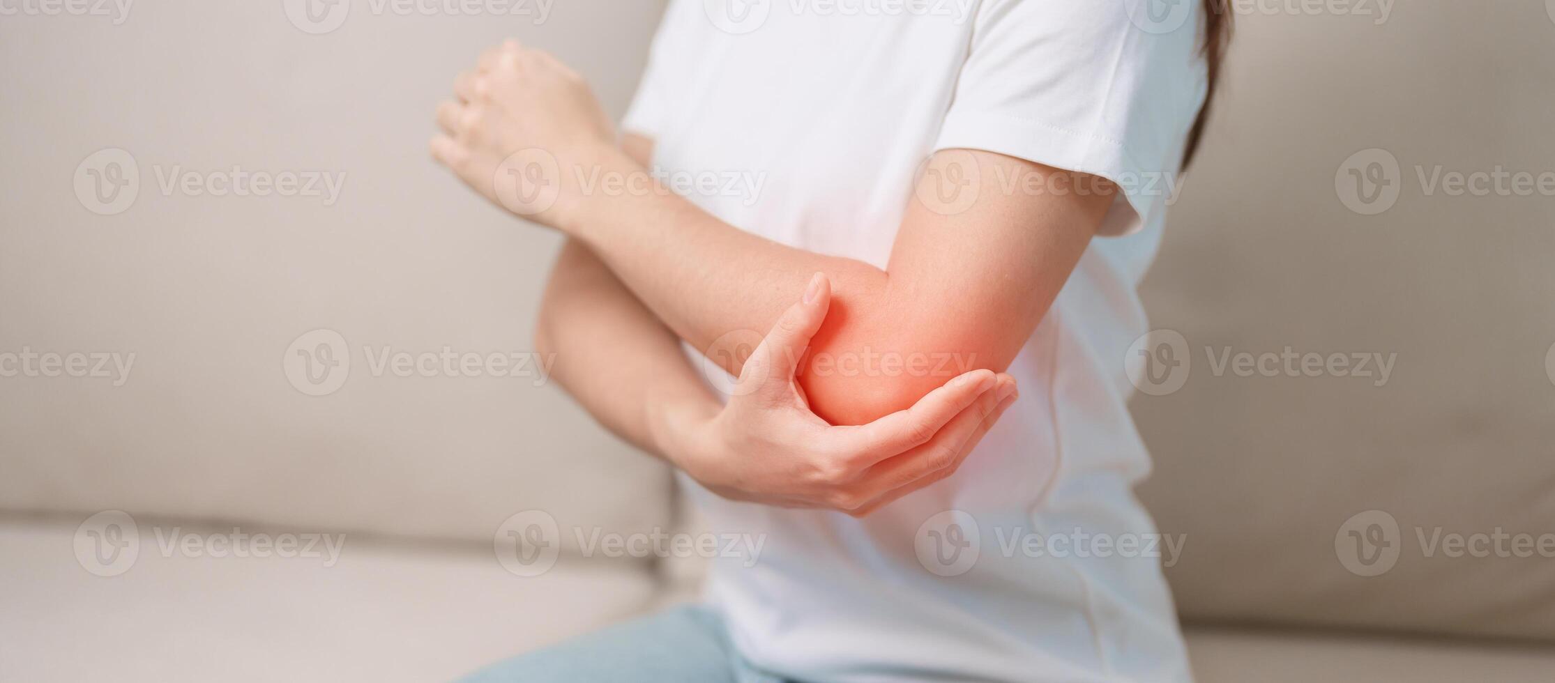 Woman having elbow ache during sitting on couch at home, muscle pain due to lateral epicondylitis or tennis elbow. injury, Health and medical concept photo