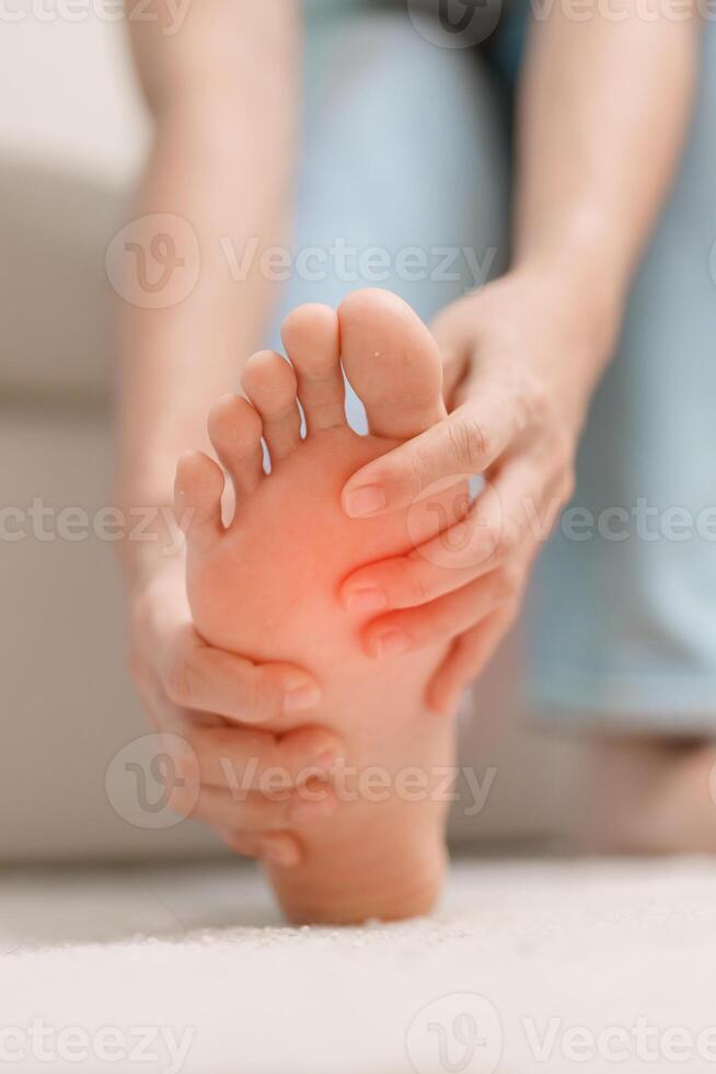 mujer teniendo descalzo dolor durante sentado en sofá a hogar. pie dolor debido a plantar fascitis y despertar largo tiempo. salud y médico concepto foto