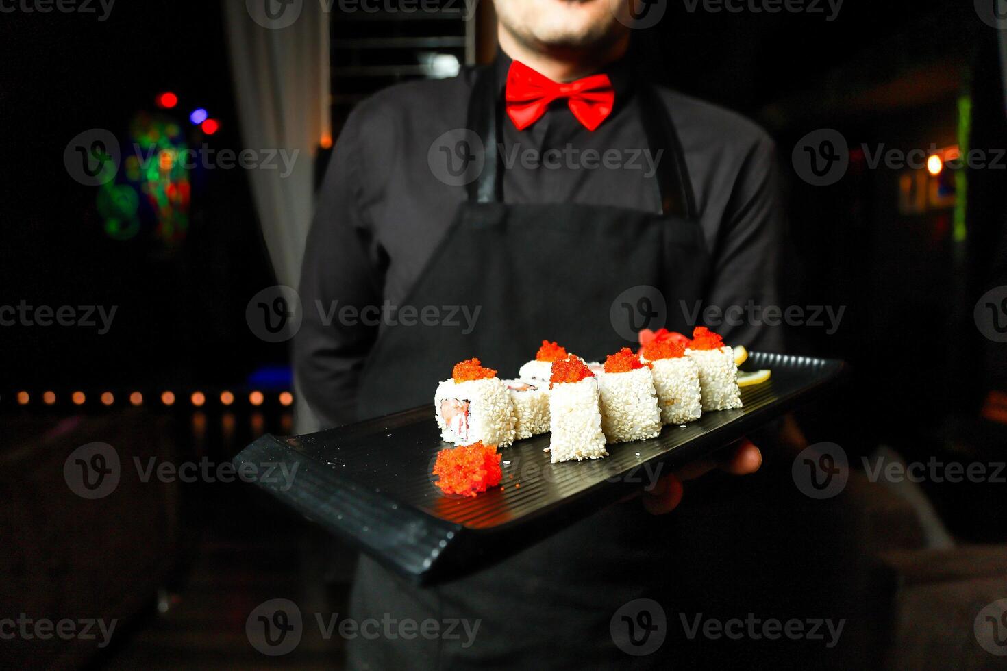hombre en negro camisa y rojo arco Corbata participación bandeja de Sushi foto