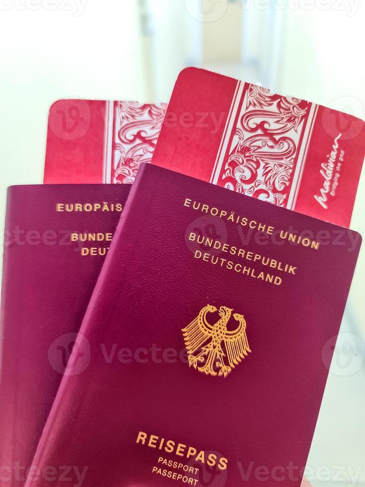 A hand holds two German passports in front of a soft travel background with boarding passes to the Maldives. photo