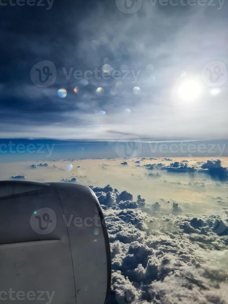 View from an airplane window of the sun and great cloud formations with many small spots on the window. photo