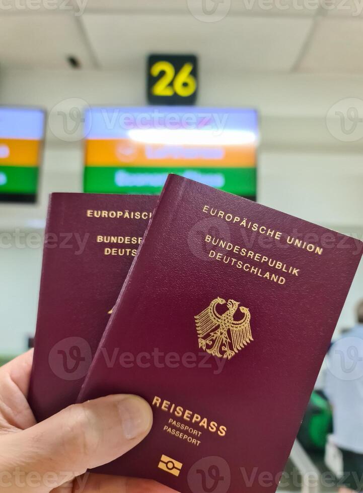 un mano sostiene dos alemán pasaportes en frente de un suave viaje aeropuerto antecedentes en vacaciones. foto