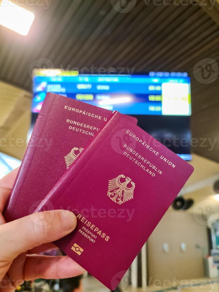 A hand holds two German passports in front of a soft travel airport background on vacation. photo
