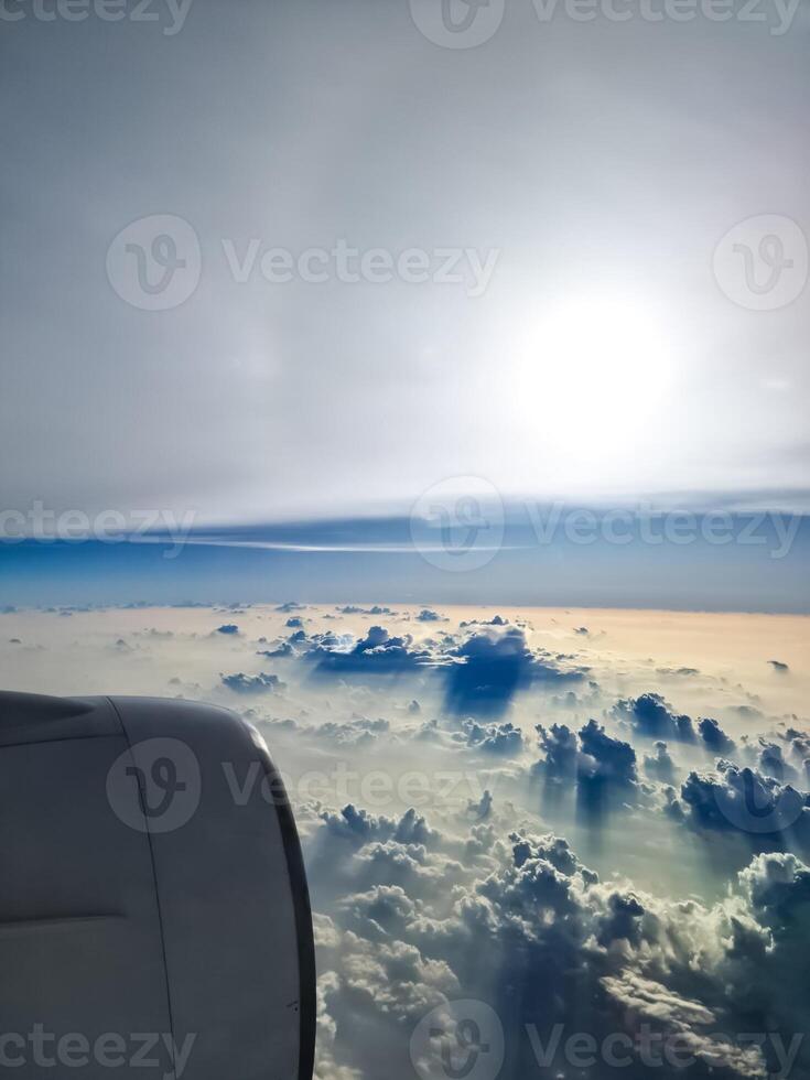 View from an airplane window of the sun and great cloud formations with many small spots on the window. photo