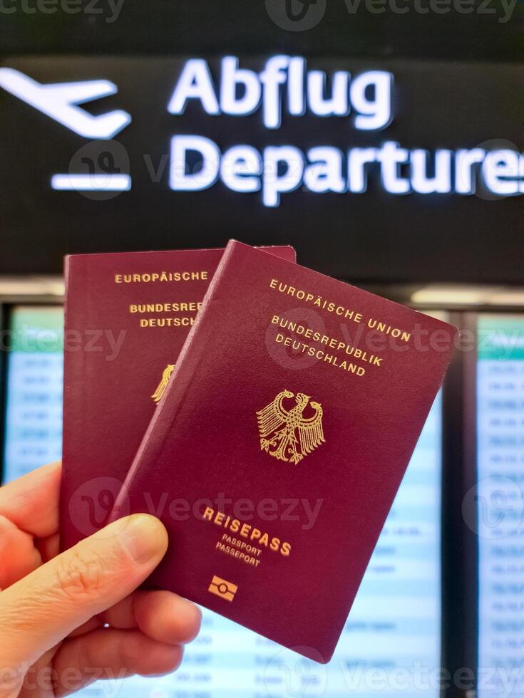 A hand holds two German passports in front of a soft travel airport background on vacation. photo