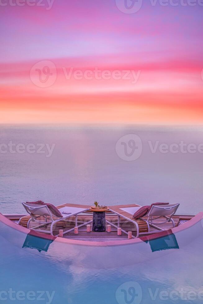 Summer love and romance table set-up for a romantic dinner meal with infinity pool reflection chairs under sunset sky and sea in the background. Luxury destination dining, romantic dinner for couples photo