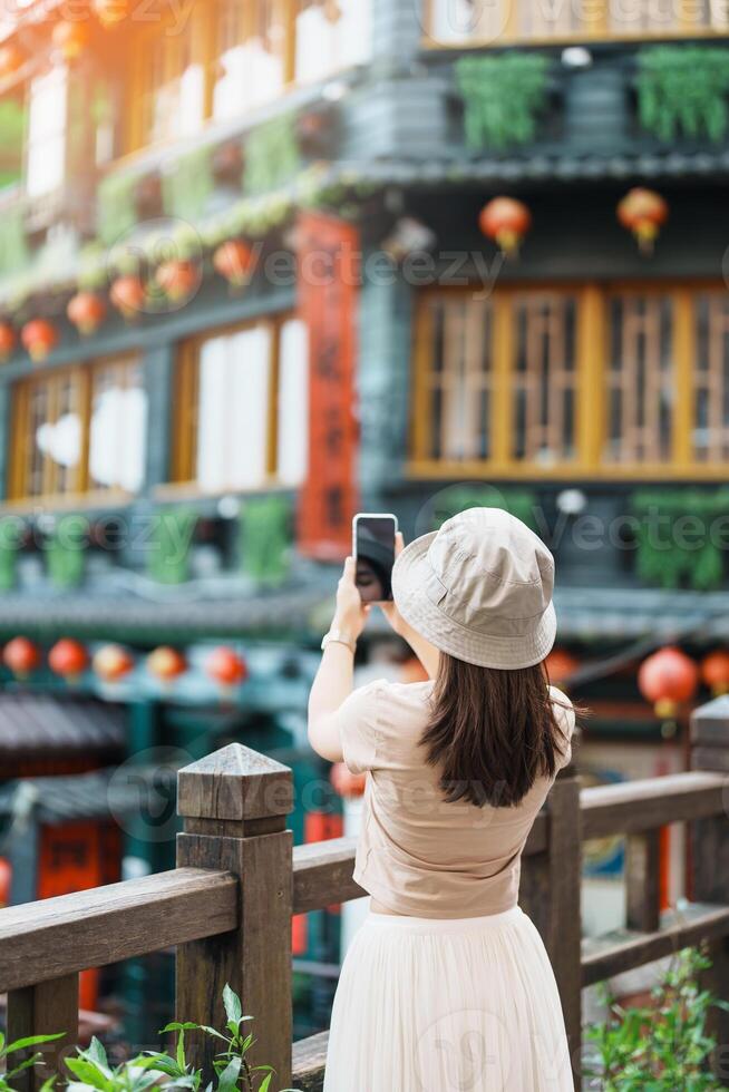 woman traveler visiting in Taiwan, Tourist taking photo and sightseeing in Jiufen Old Street village with Tea House background. landmark and popular attractions near Taipei city. Travel concept