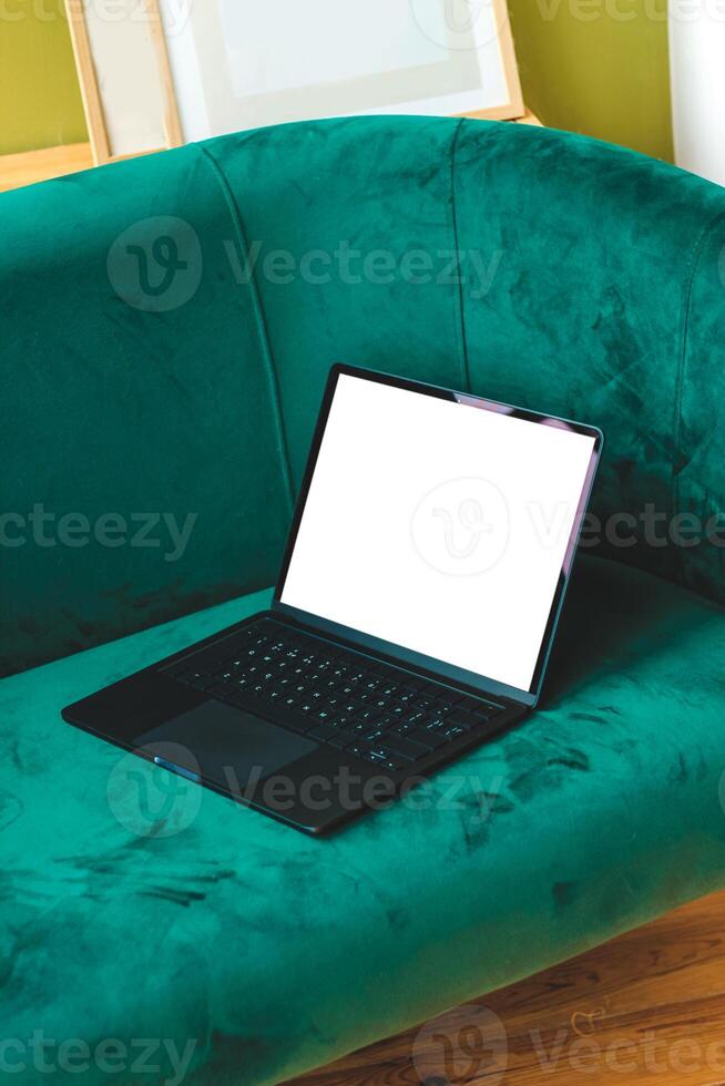 A thin laptop working computer stands on a stylish green sofa in the interior. photo