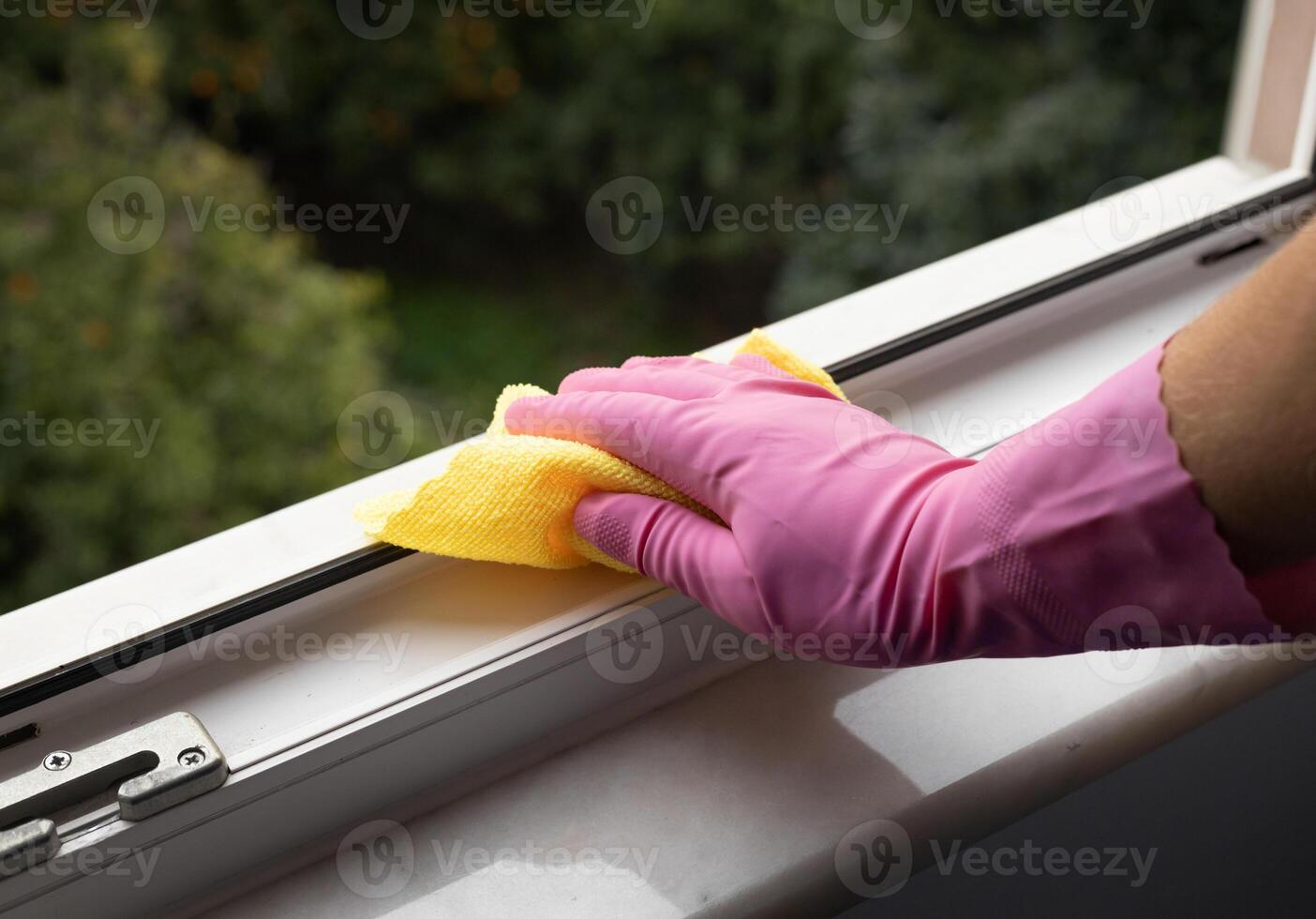 Hand holding a yellow microfiber cloth to clean dust on a window rail. High quality photo