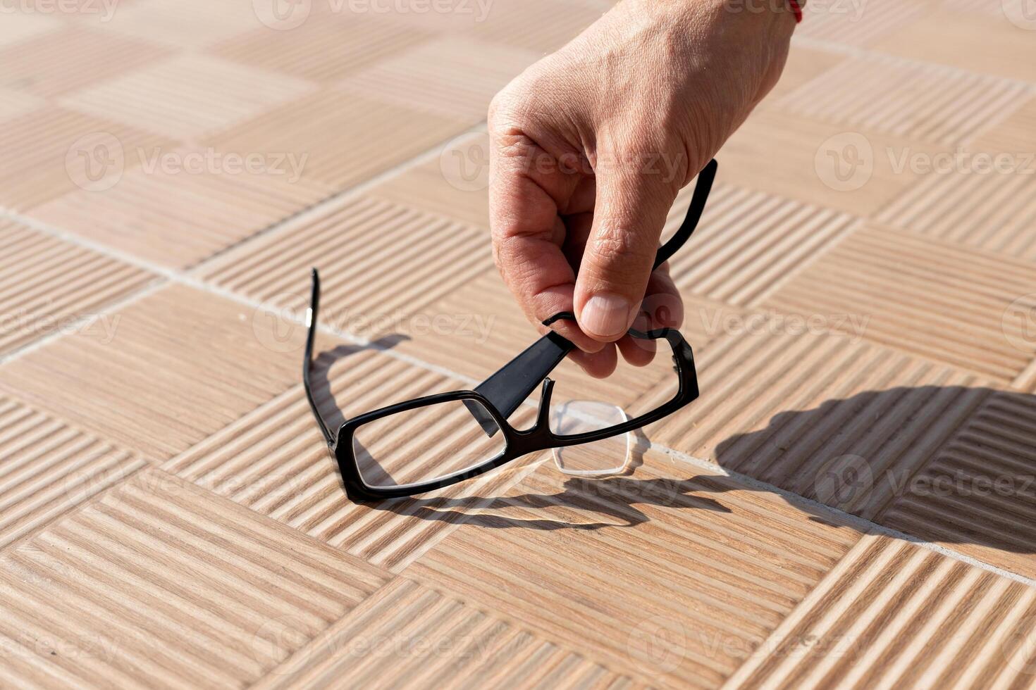 the hand of an unknown person picks up a broken spectacle frame on the street from a tile. High quality photo