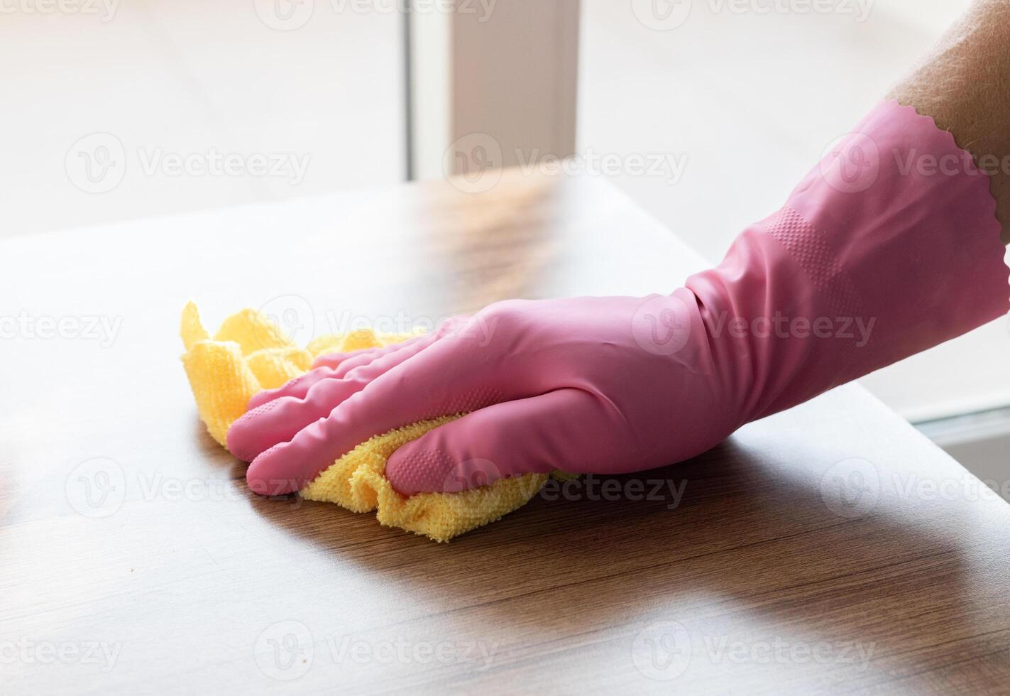 a hand in a pink glove wipes the surface of a wooden table with yellow microfiber. High quality photo