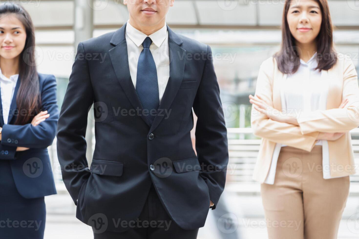 Businessman standing with hands in pocket over blurry team background photo