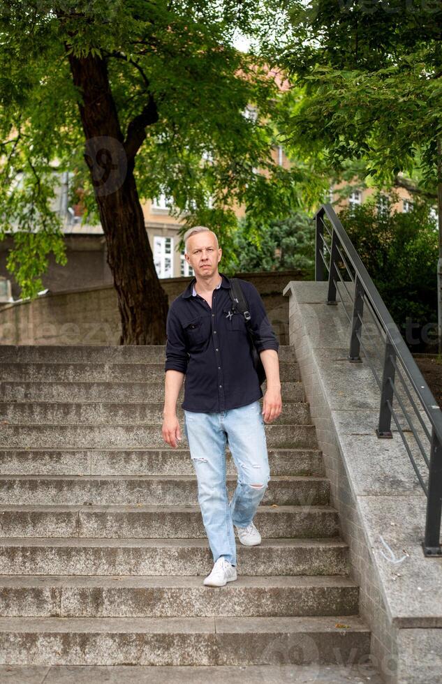 canoso joven hombre con un mochila va abajo el escalera en el parque. alto calidad foto