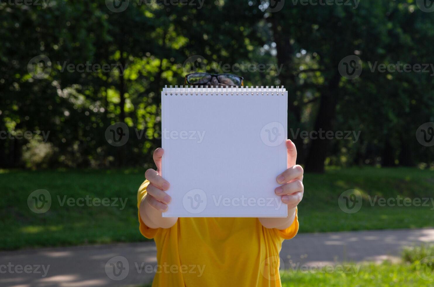 young woman in yellow t shirt holding a white book in front of her in the park on a sunny summer day. background is blurred. selective focus. High quality photo