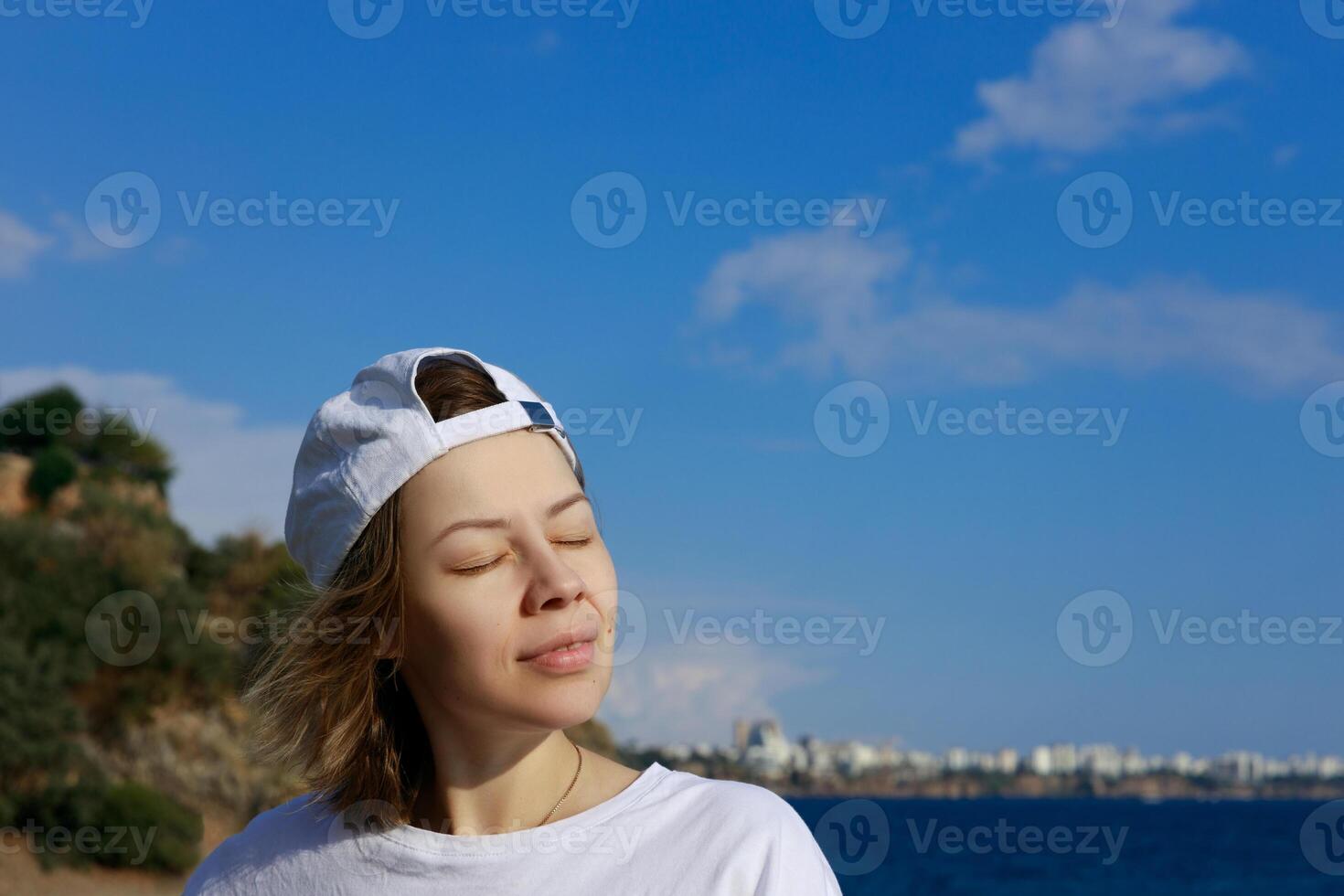 el niña convertido su cara a el Dom y toma el sol. en contra el azul cielo.volver ver de el costa. alto calidad foto