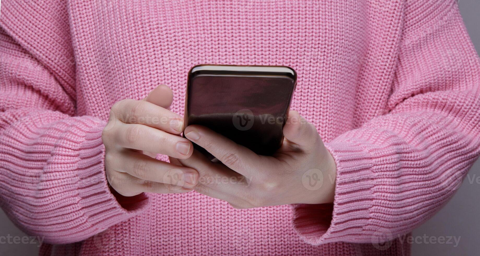 manos un niña en un rosado suéter participación un negro teléfono inteligente alto calidad foto