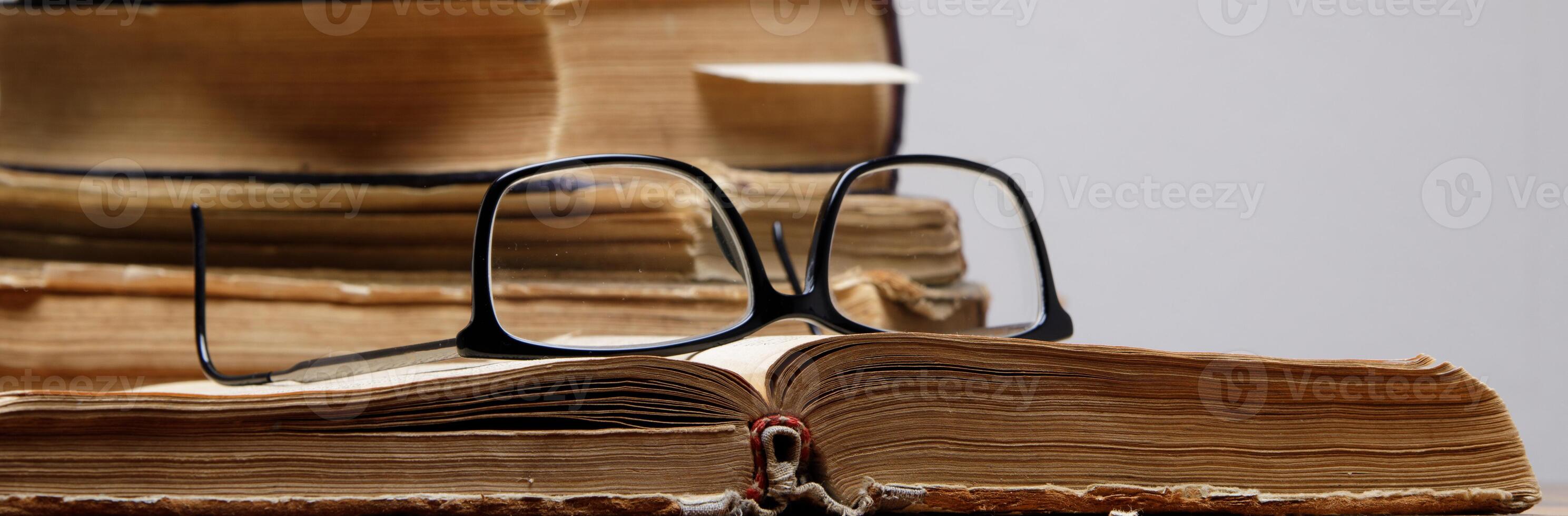 a stack of old books with bookmarks on a wooden table on a gray background. glasses lie on an open book.selective focus photo