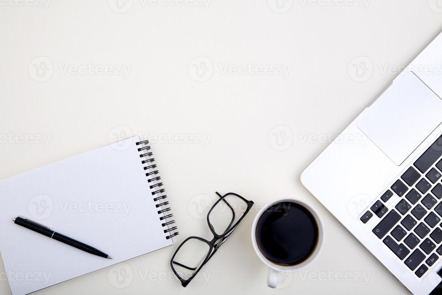 light office desk with laptop, white notebook mockup, glasses and coffee cup. Top view with copy space for text input. photo