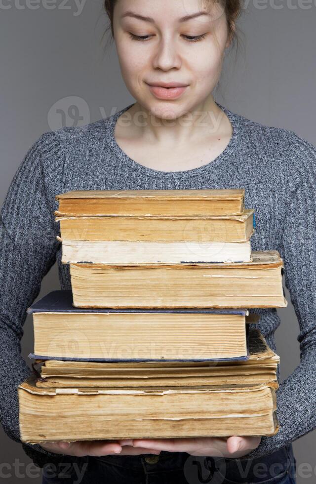 young female student looking and smiling looking at a book. holds many old books in her hands photo