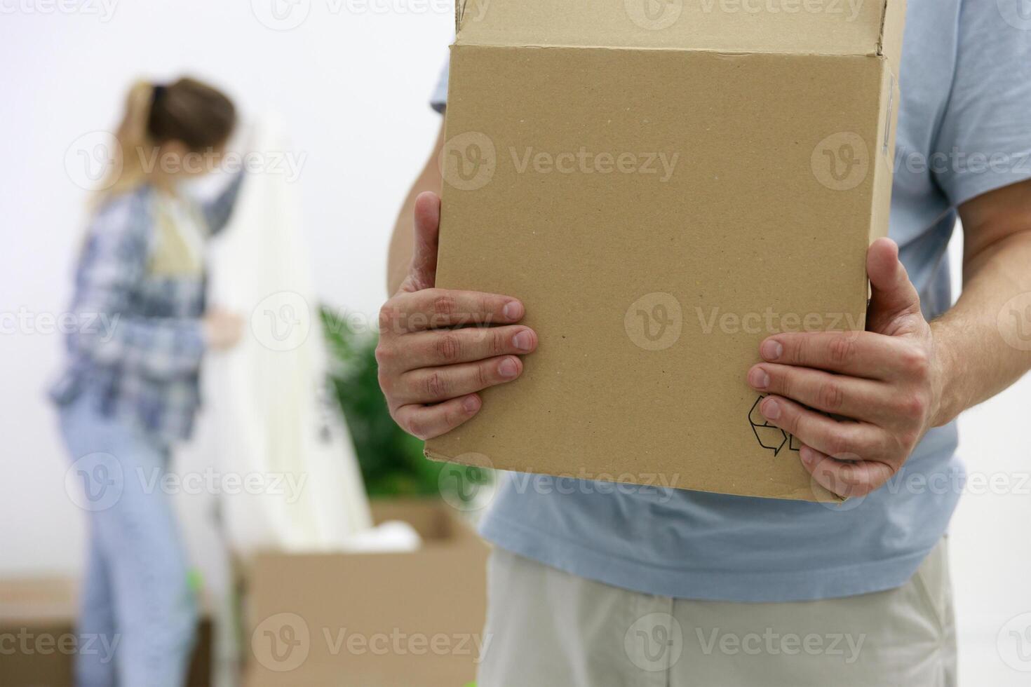 Close-up of a man with cardboard boxes moving into a new house. in the background a girl unpacks things. out of focus. High quality photo