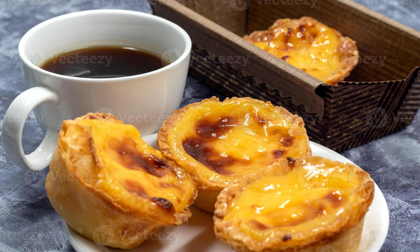 Lots of desserts Pastel de nata or Portuguese egg tart with a white cup of black coffee. Pastel de Belm is a small pie with a crispy puff pastry crust and a custard cream filling. photo
