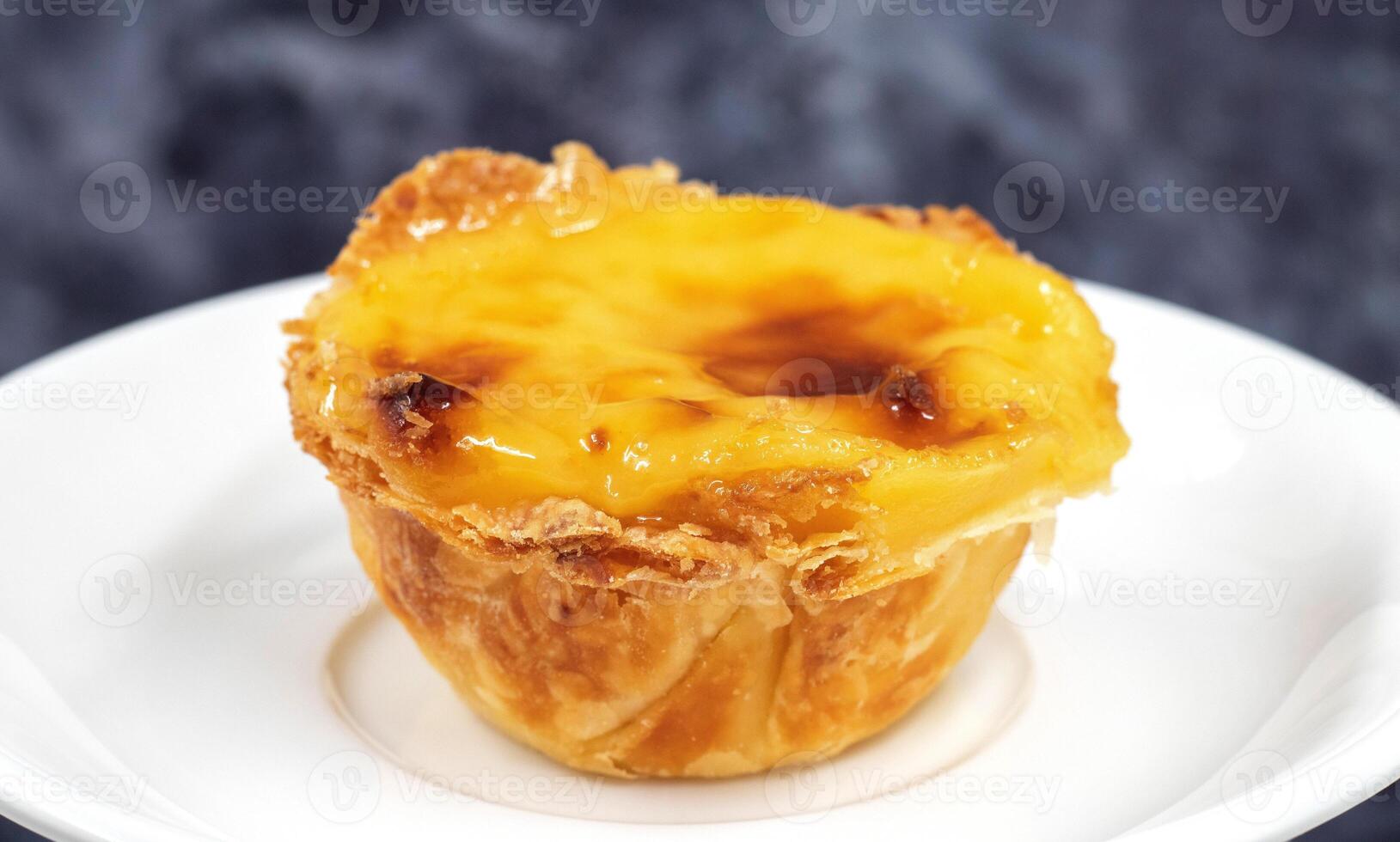One Pastel de nata or Portuguese egg tart on a white plate. Pastel de Belm is a small pie with a crispy puff pastry crust and a custard cream filling. photo