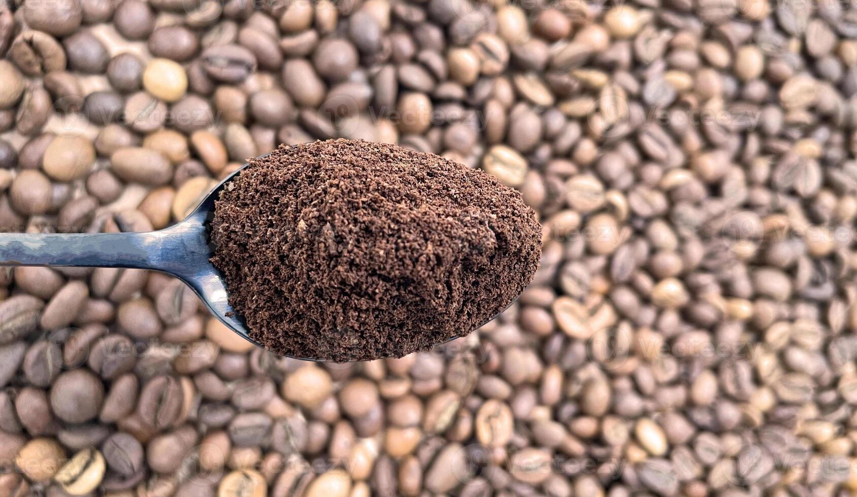 Ground coffee powder in a metal spoon in the foreground, against the background of roasted aromatic coffee beans. Coffee concept. photo