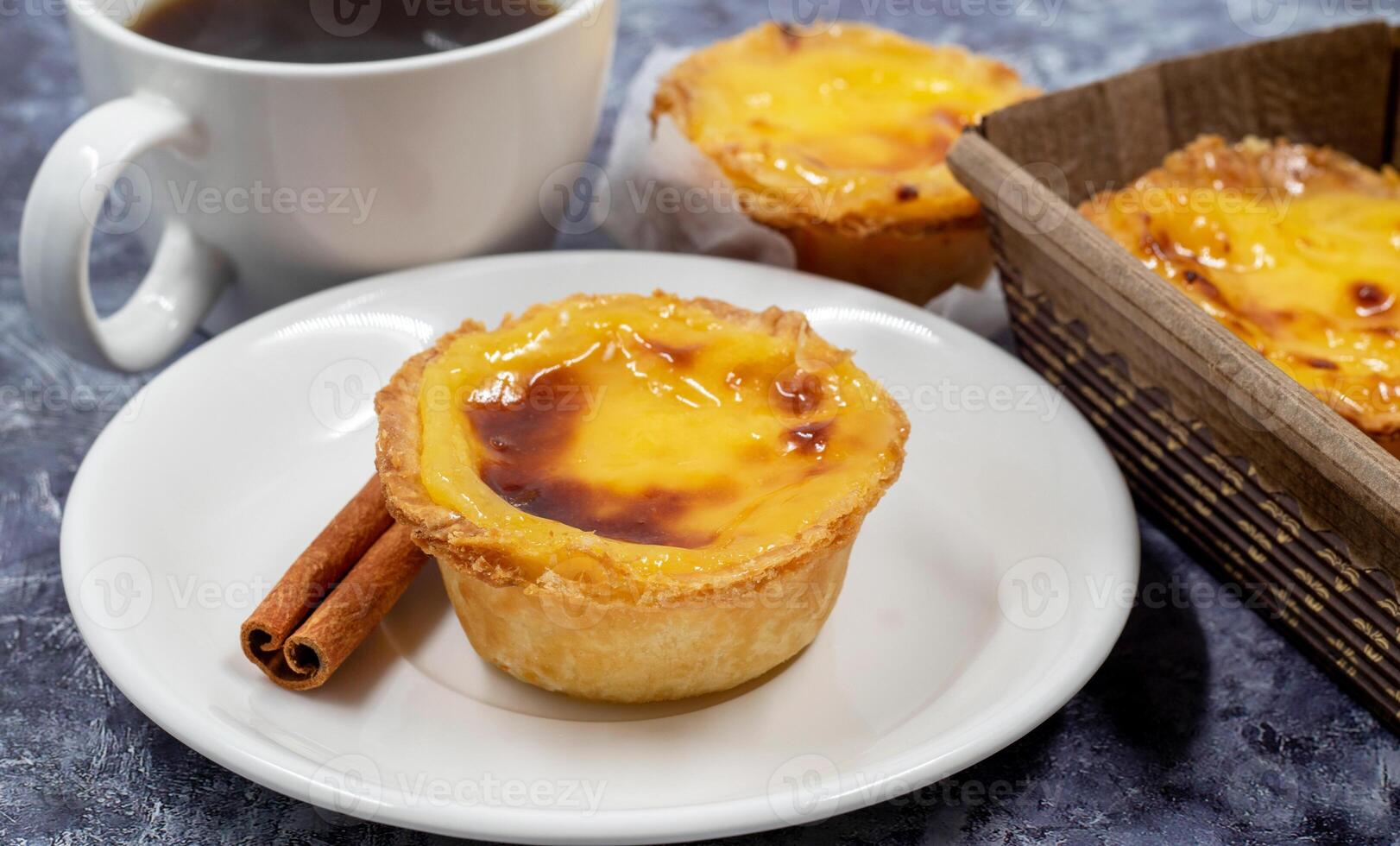 Lots of desserts Pastel de nata or Portuguese egg tart and cinnamon sticks with a cup of coffee. Pastel de Belm is a small pie with a crispy puff pastry crust and a custard cream filling. photo