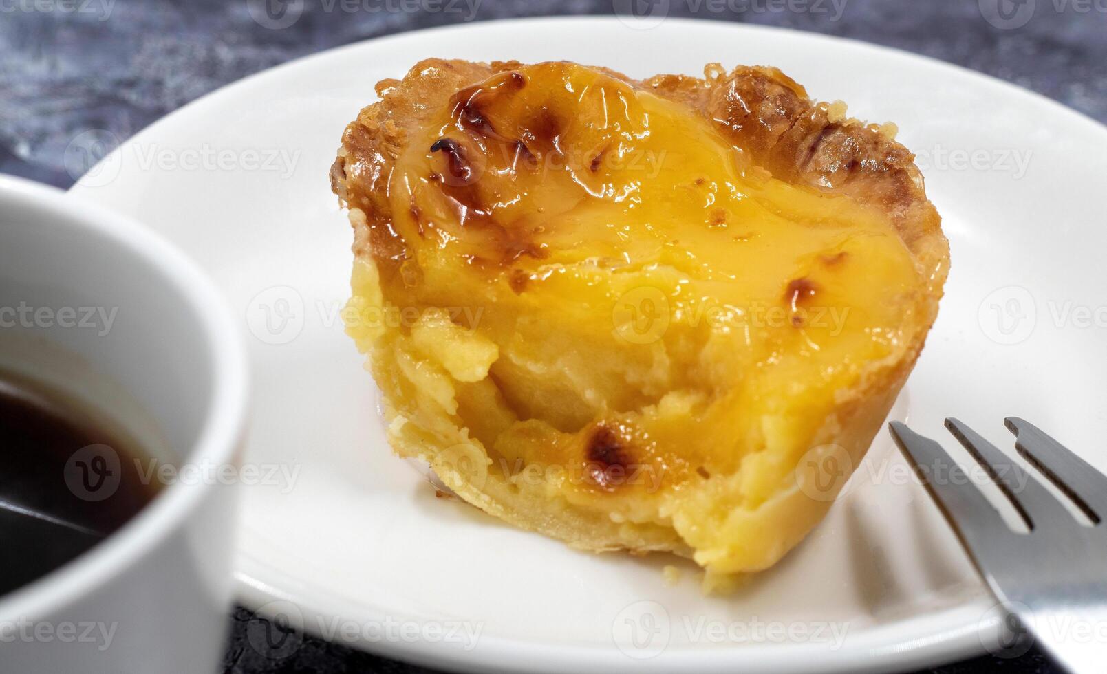 One Pastel de nata or Portuguese egg tart on a white plate. Pastel de Belm is a small pie with a crispy puff pastry crust and a custard cream filling. photo