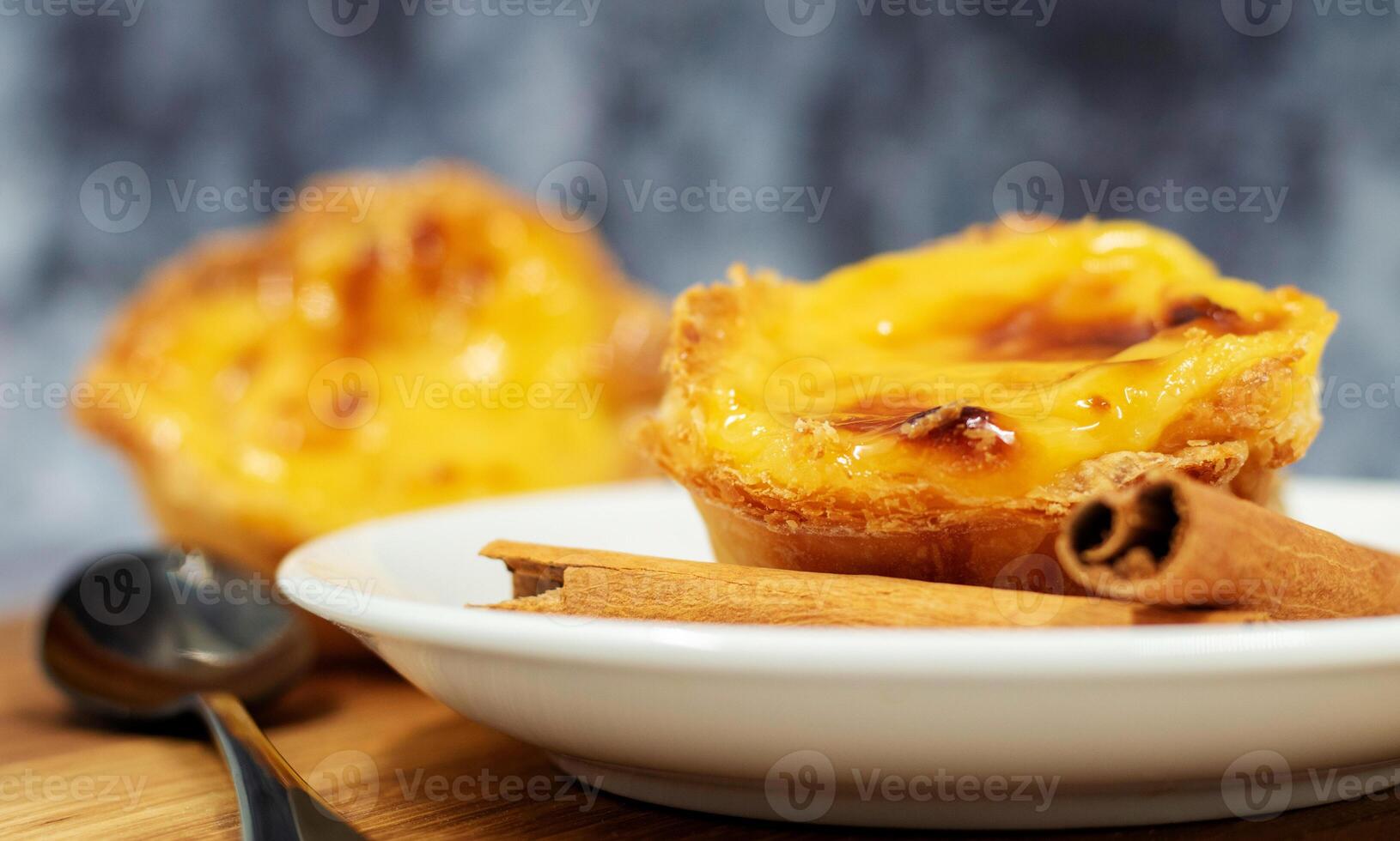 Three Pastel de nata or Portuguese egg tart and cinnamon sticks on a wooden brown background. Pastel de Belem is a small dessert, a cup-shaped pastry made from puff pastry with custard. photo