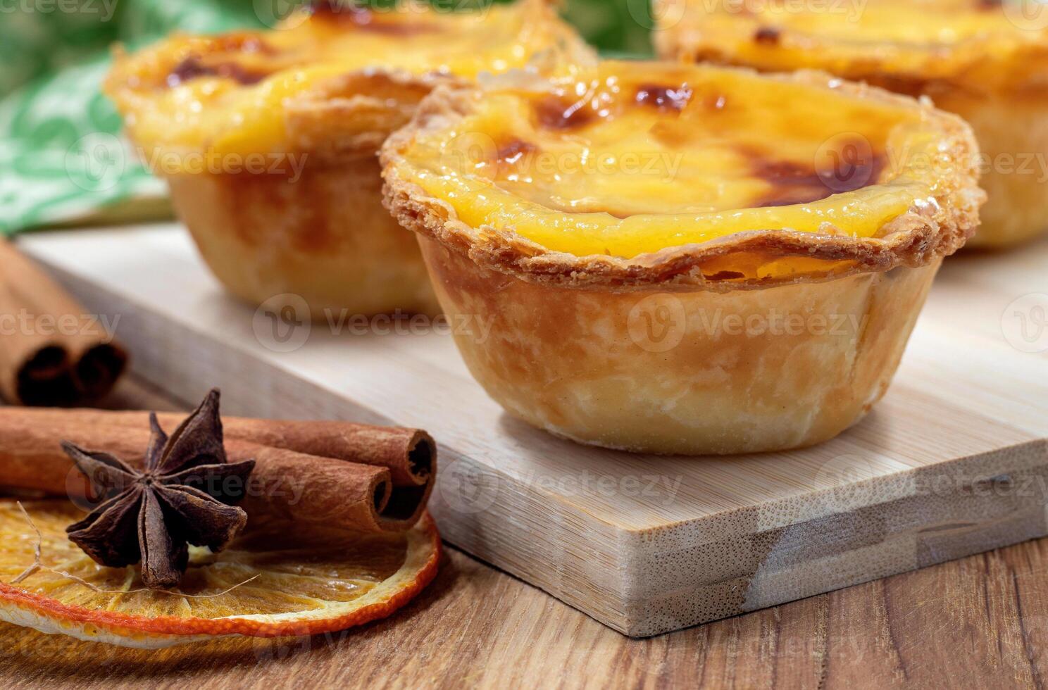 Lots of desserts Pastel de nata or Portuguese egg tart and cinnamon sticks. Pastel de Belm is a small pie with a crispy puff pastry crust and a custard cream filling. photo