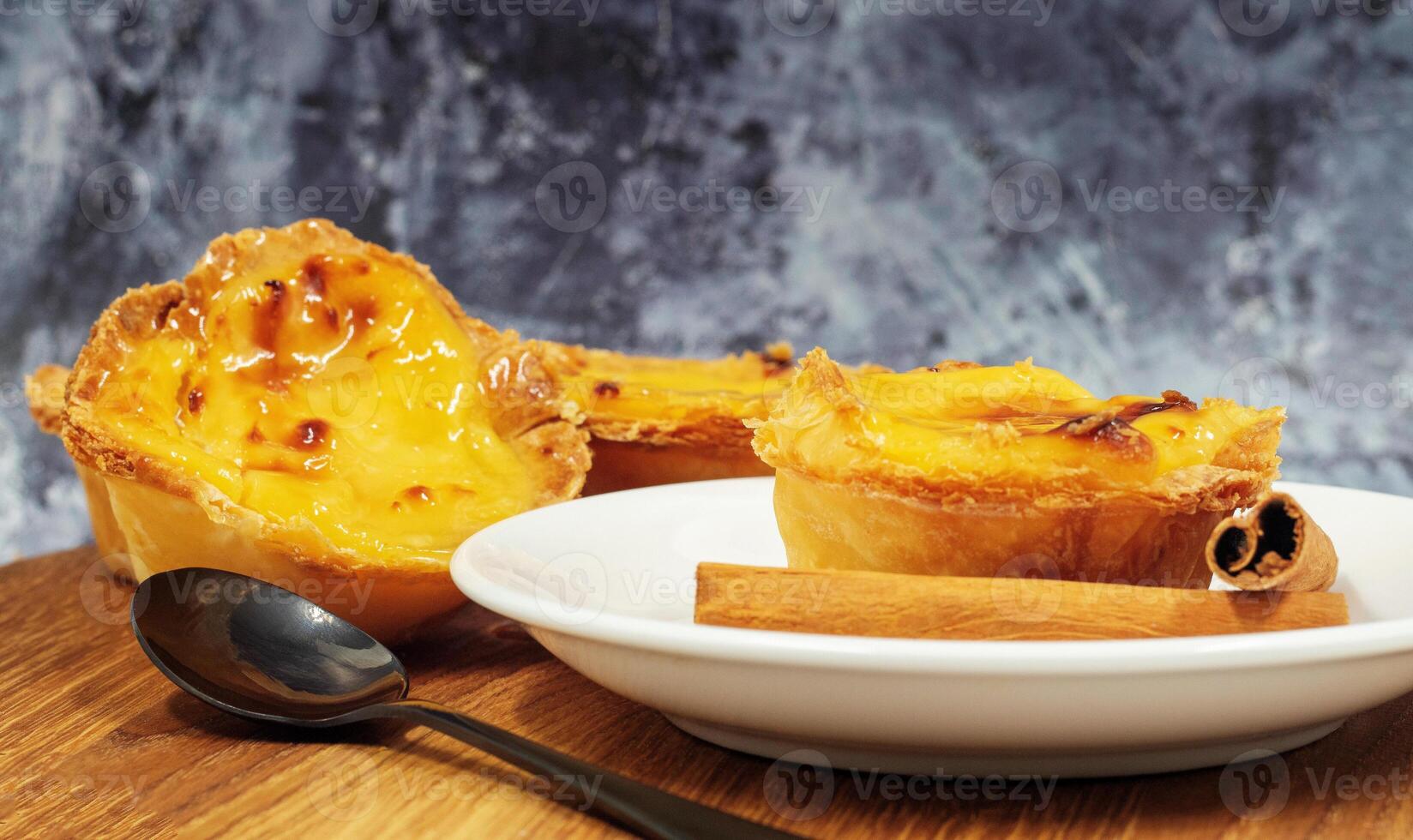 Pastel de nata tarts or Portuguese egg tart and cinnamon sticks on a wooden brown background. Pastel de Belem is a small pie with a crispy puff pastry crust and a custard cream filling. photo
