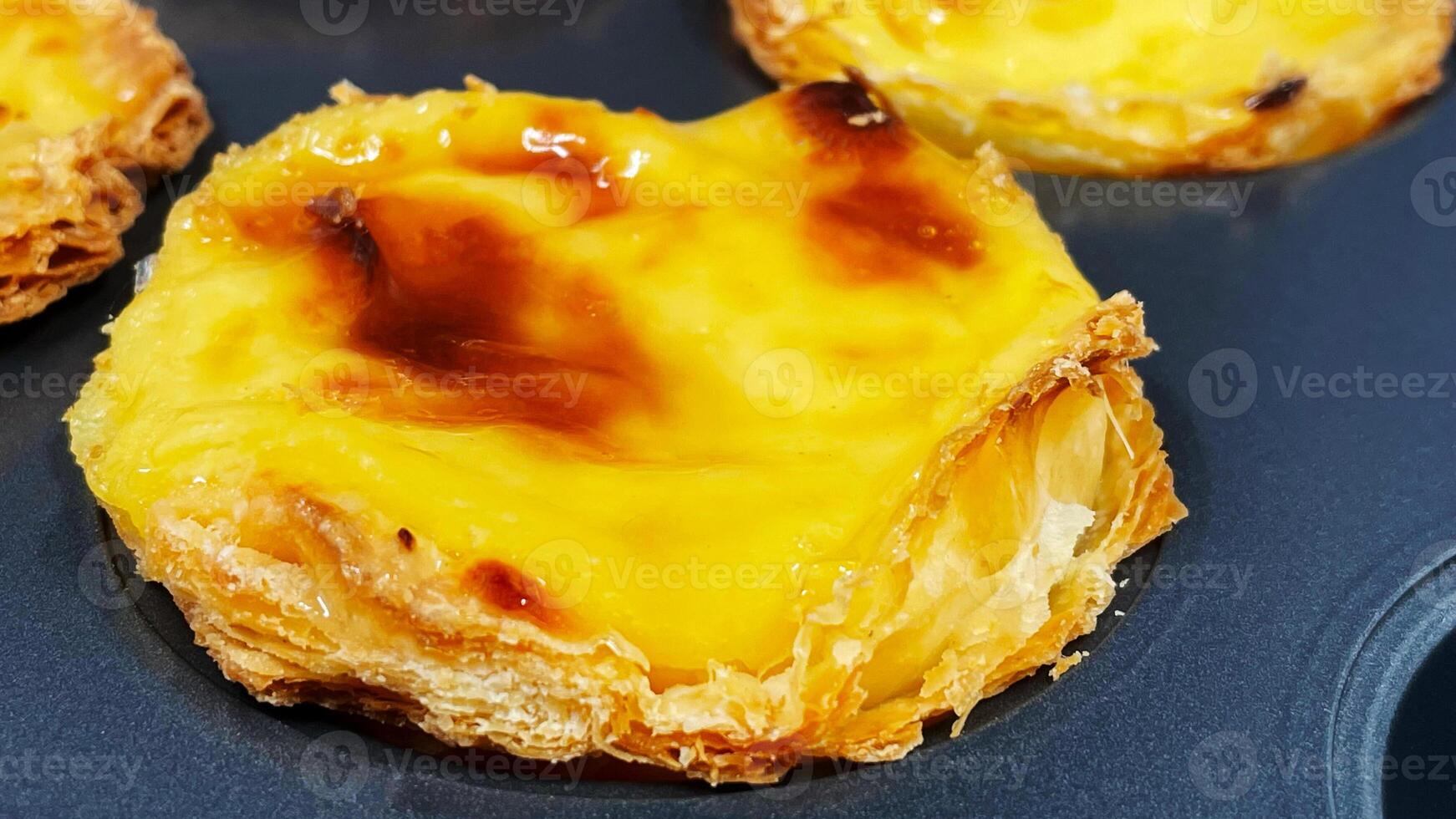 Lots of freshly baked Pastel de nata or Portuguese egg tart desserts in a baking dish. Pastel de Belme is a small pie with a crispy puff pastry crust and a custard filling. Small cupcake. photo