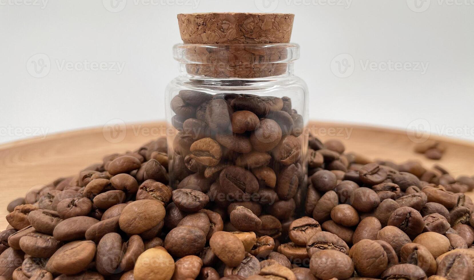Coffee beans in a small glass jar with a cork lid on the table. Coffee beans packed in a transparent, airtight storage container. Coffee seeds inside a glass jar. photo