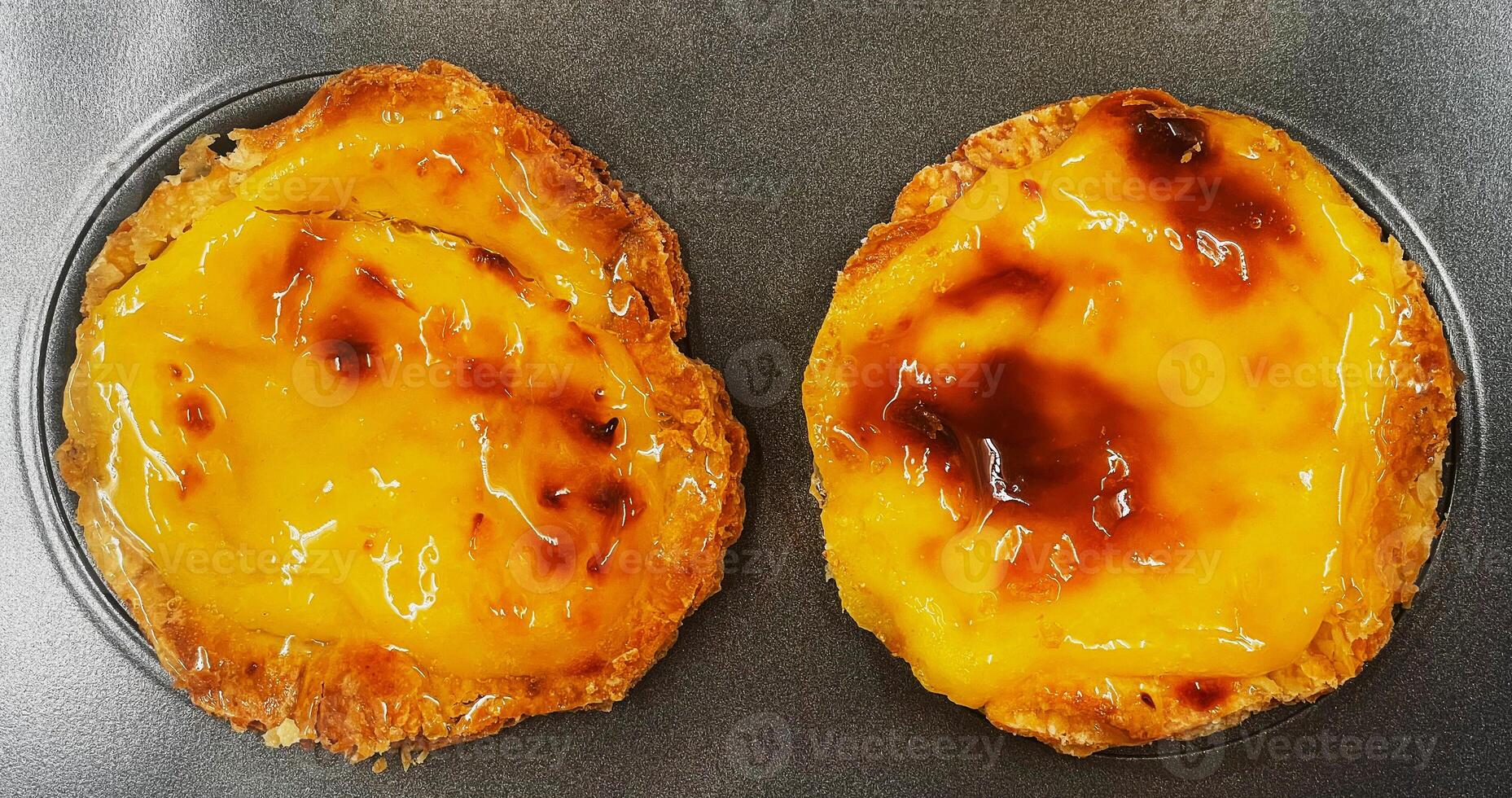 Two freshly baked Pastel de nata or Portuguese egg tart desserts in a baking dish. Pastel de Belm is a small pie with a crispy puff pastry crust and a custard cream filling. photo