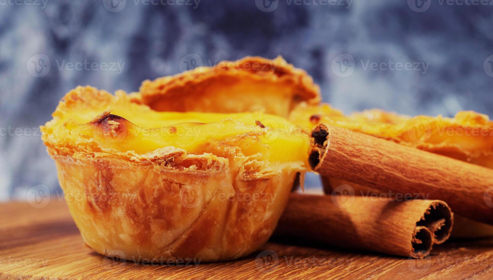 Three Pastel de nata or Portuguese egg tart and cinnamon sticks on a wooden brown background. Pastel de Belem is a small dessert, a cup-shaped pastry made from puff pastry with custard. photo