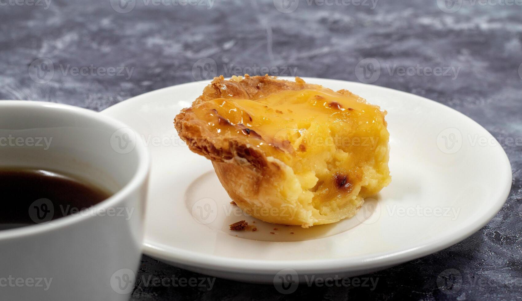 One uneaten Pastel de nata or Portuguese egg dessert on a white plate. Pastel de Belm is a small pie with a crispy puff pastry crust and a custard cream filling. Eating a small dessert, a cupcake. photo