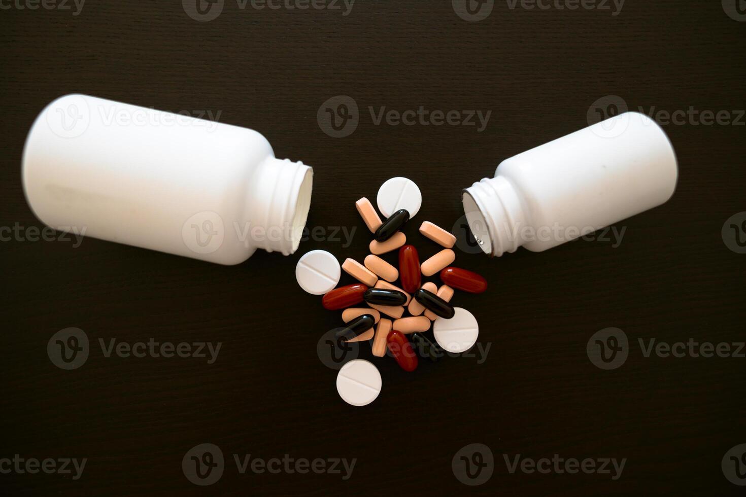 Two white jars with scattered red, pink and black medicines on a dark table. photo