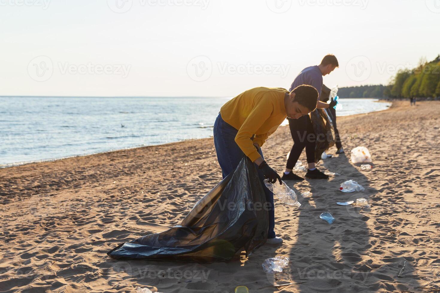 Earth day. Volunteers activists collects garbage cleaning of beach coastal zone. Woman and mans puts plastic trash in garbage bag on ocean shore. Environmental conservation coastal zone cleaning photo