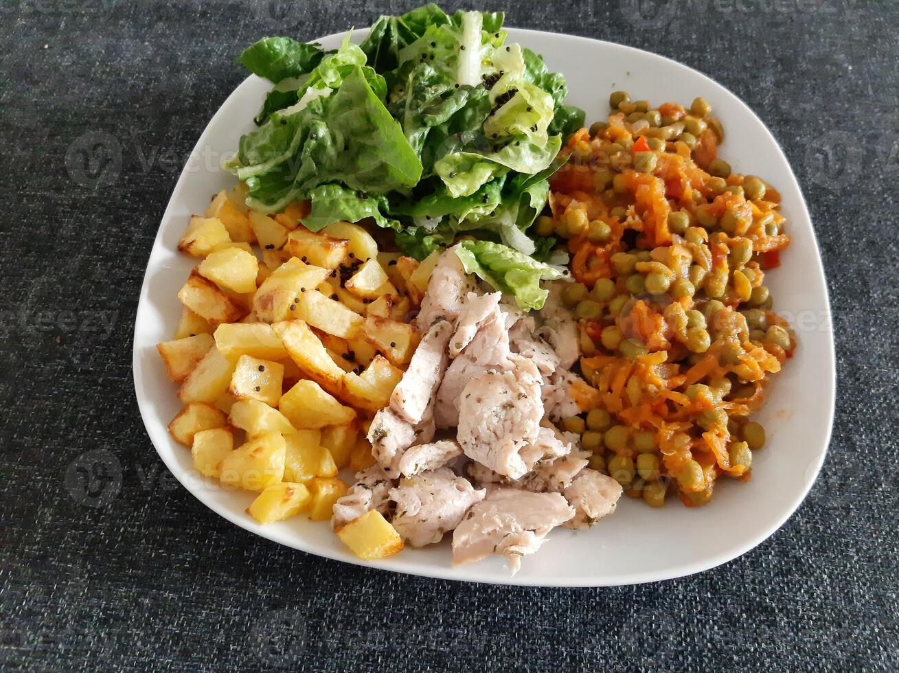 hecho en casa A la parrilla pollo con francés papas fritas, verde ensalada y guisante estofado servido en un blanco plato foto