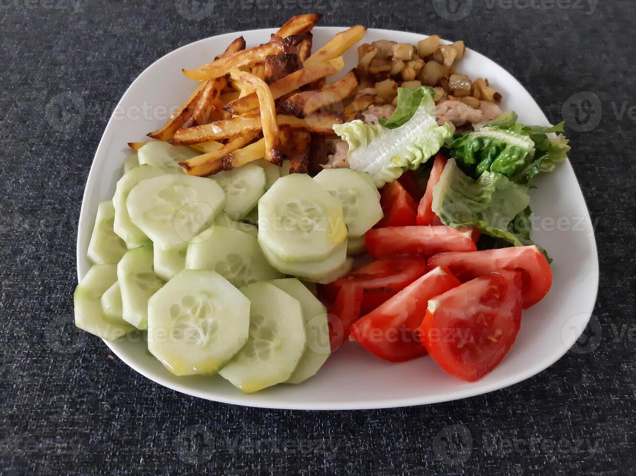 Homemade grilled chicken with french fries, cucumber, sliced tomato and green salad, served on a white plate photo