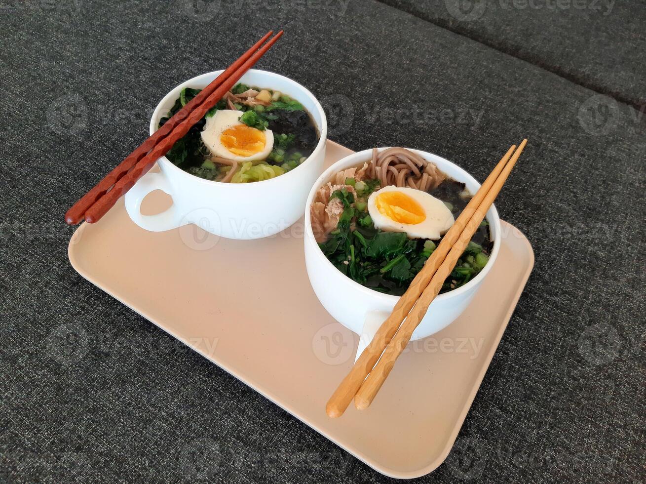 Asian ramen soba noodle soup close up with chicken, boiled egg, nori, green spinich and green onion served with chopsticks photo