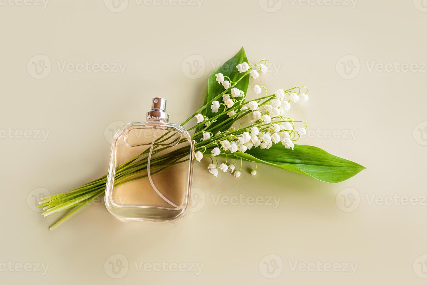 A transparent bottle of perfume with a delicate aroma of spring lilies of the valley lies on a bouquet of flowers. Pastel background. photo